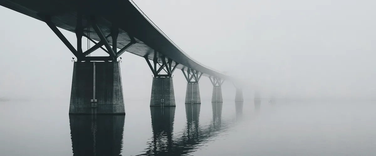 A long concrete bridge crossing still water and fading into fog